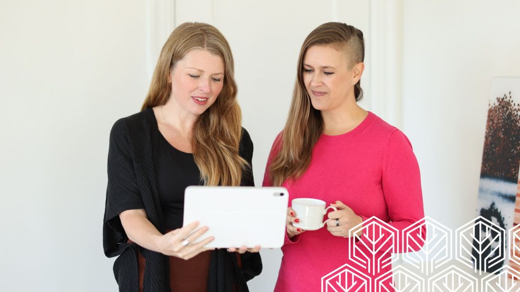 Julia showing her Ipad to Stefanie who holding a cup of coffee