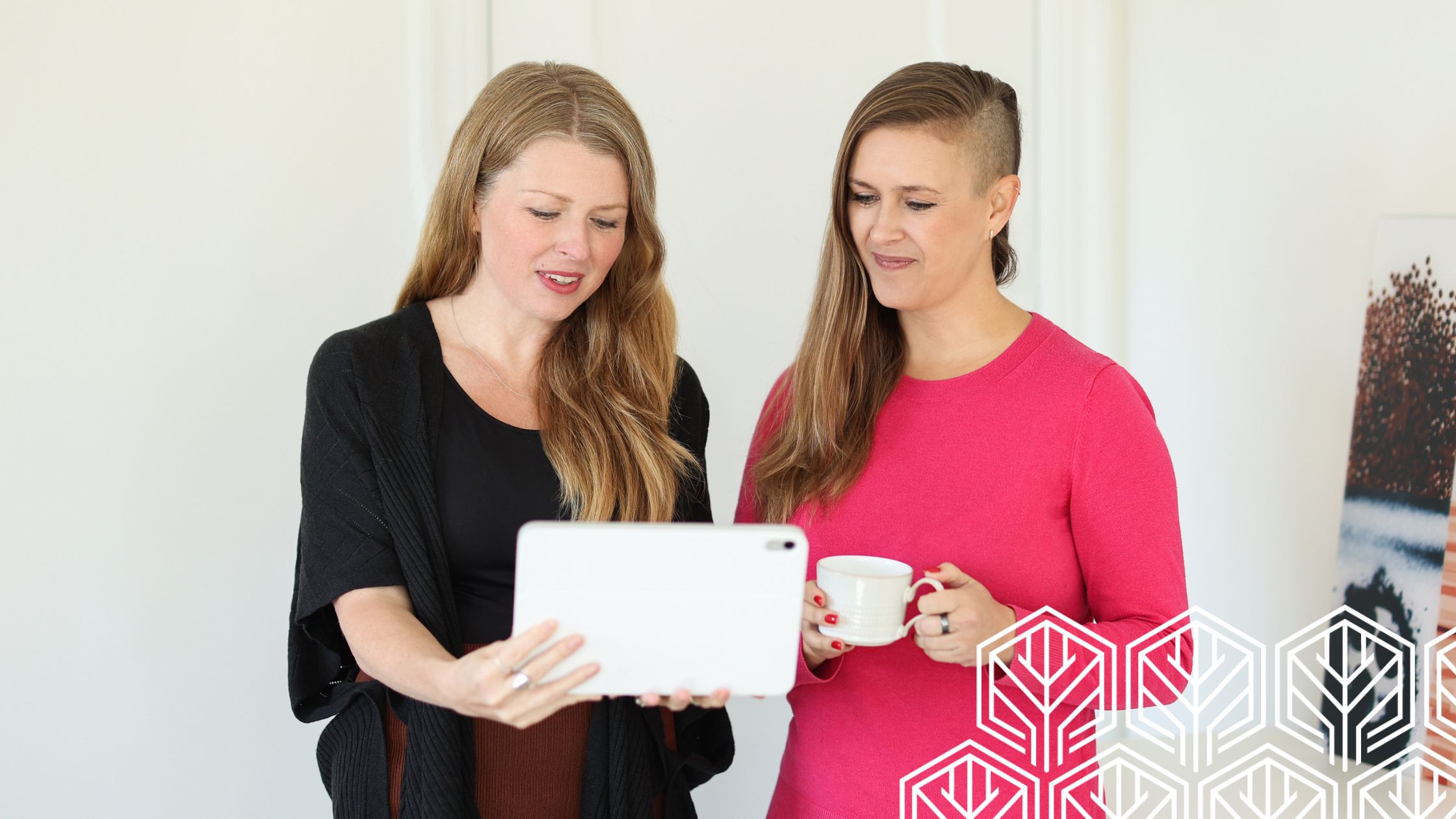 Julia showing her Ipad to Stefanie who holding a cup of coffee