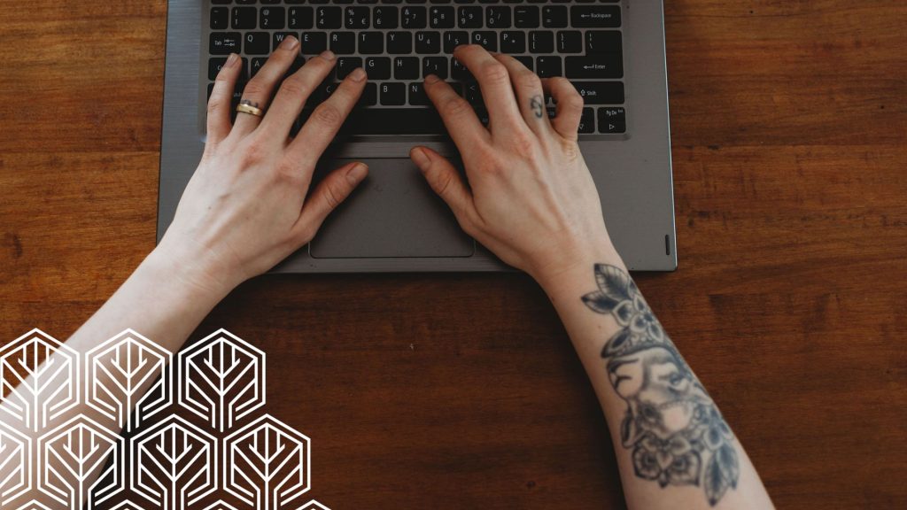 an image of hands with a tattoo typing on a laptop