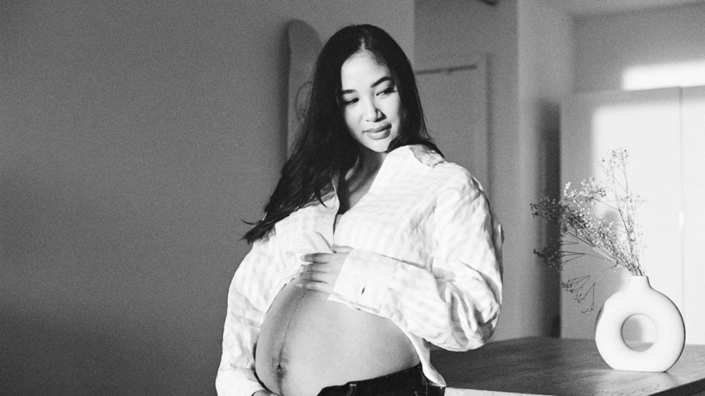 black haired woman in longsleeves showing her pregnant belly